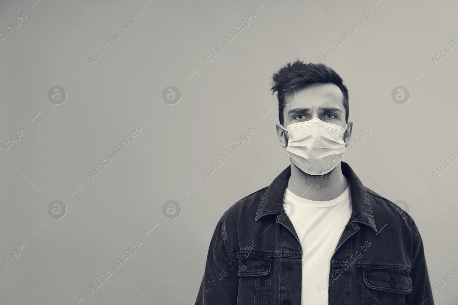 Image of Man wearing medical face mask on light background, space for text. Black and white photography