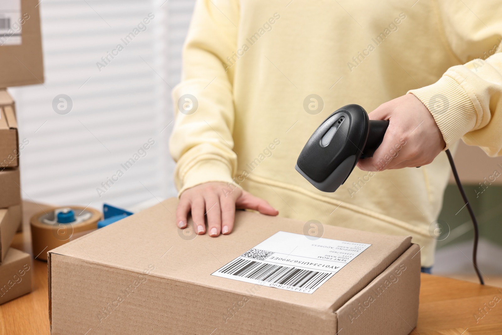 Photo of Parcel packing. Post office worker with scanner reading barcode indoors, closeup