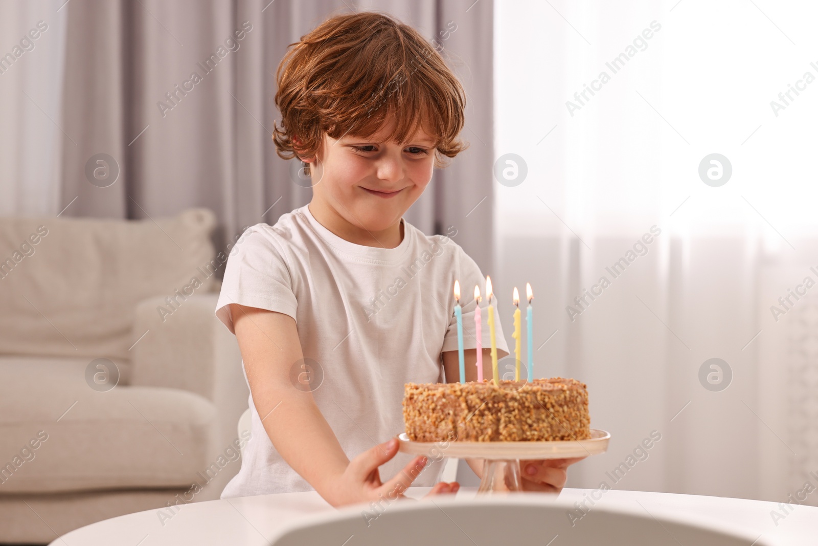 Photo of Cute boy with birthday cake at table indoors