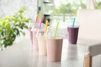 Photo of Different milk shakes in plastic cups on white wooden table indoors