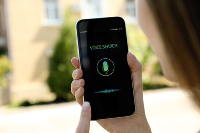 Woman using voice search on smartphone outdoors, closeup
