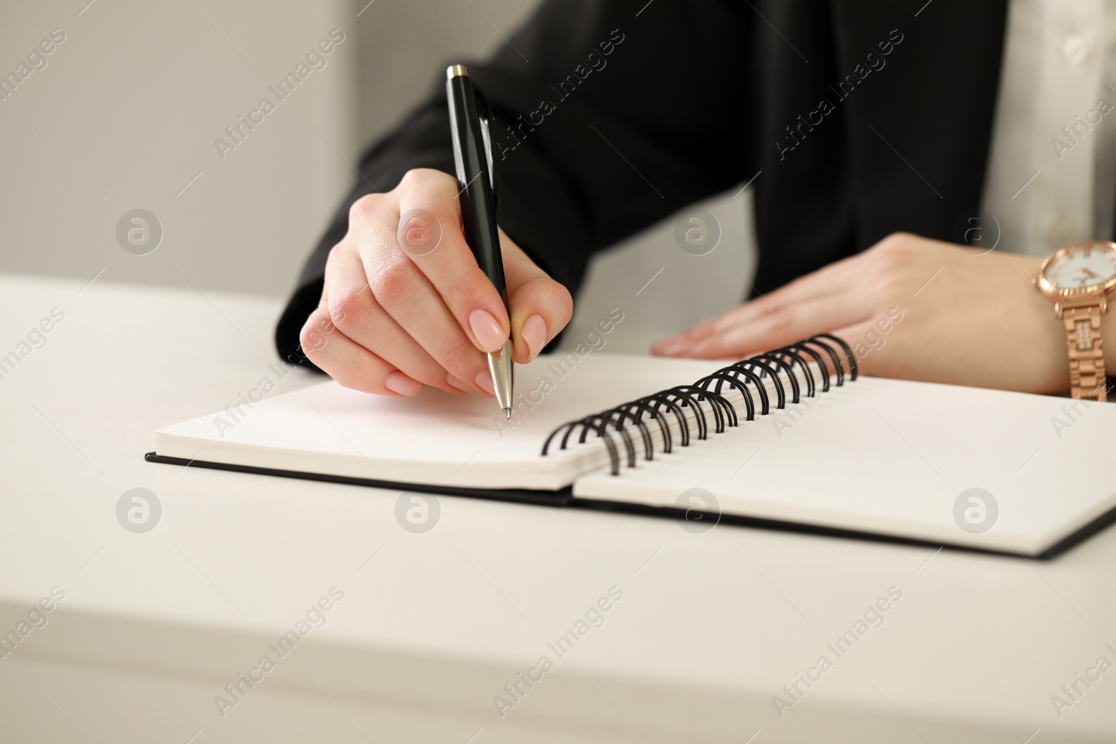 Photo of Woman writing in notebook at white table, closeup