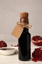 Photo of Glass bottle of pomegranate sauce and fresh ripe fruit on white marble table
