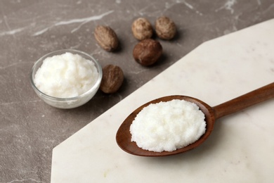 Photo of Shea butter in wooden spoon and bowl with nuts on grey background