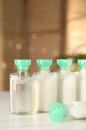 Mini bottles of cosmetic products on white table against blurred background, closeup