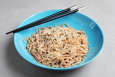 Photo of Plate of noodles with sesame and chopsticks on table, closeup