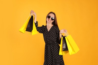 Photo of Happy young woman with shopping bags on yellow background. Big sale