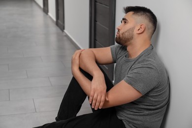 Photo of Sad man sitting on floor in hall. Space for text