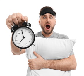 Photo of Emotional overslept man with alarm clock and pillow on white background. Being late concept