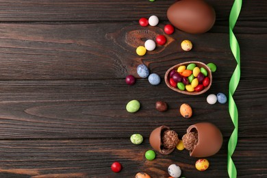 Tasty chocolate eggs and sweets on wooden table, flat lay. Space for text