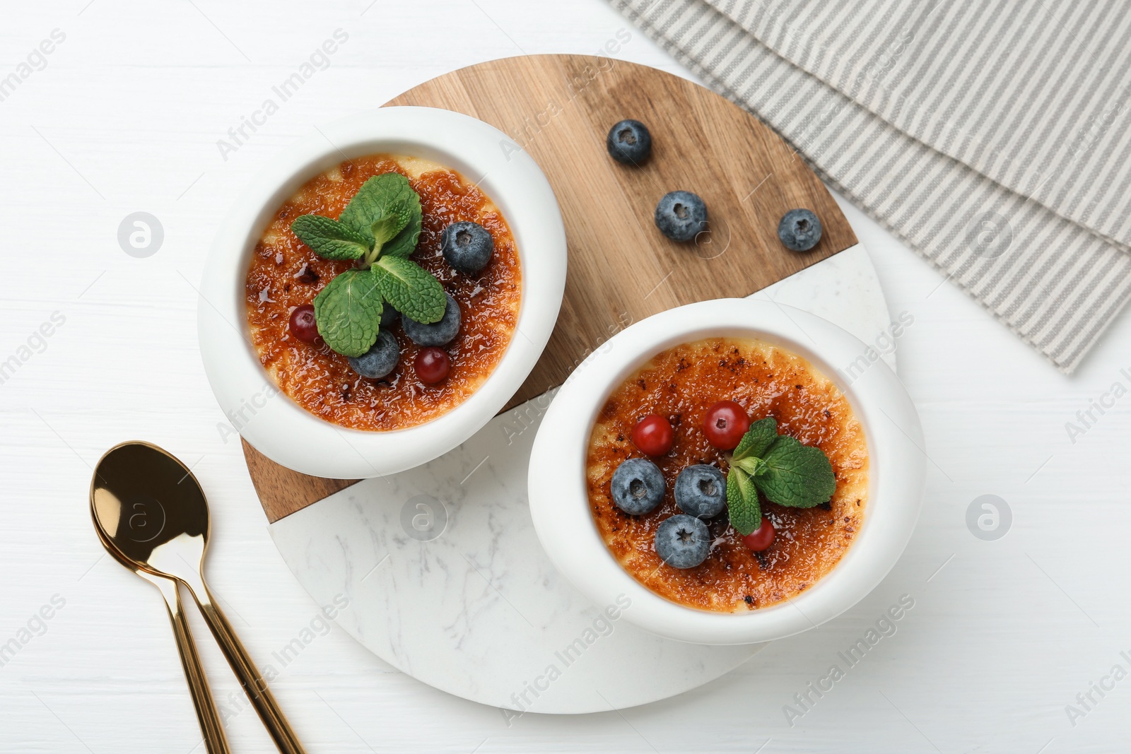 Photo of Delicious creme brulee with berries and mint in bowls on white wooden table, top view
