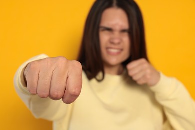 Photo of Young woman ready to fight against orange background, focus on hand. Space for text