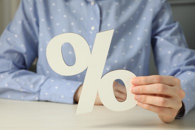 Photo of Woman holding percent sign at white wooden table, closeup