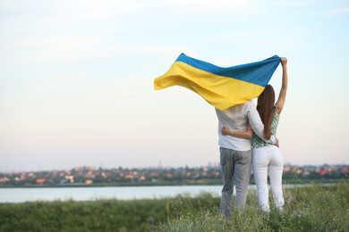Photo of Friends holding national flag of Ukraine in field, back view. Space for text