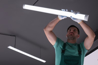 Photo of Ceiling light. Electrician installing led linear lamp indoors, low angle view
