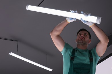 Ceiling light. Electrician installing led linear lamp indoors, low angle view