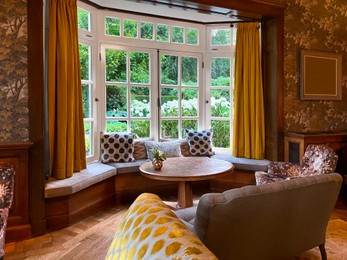 Photo of Wooden table near bay window seat with cushions in cozy room. Interior design