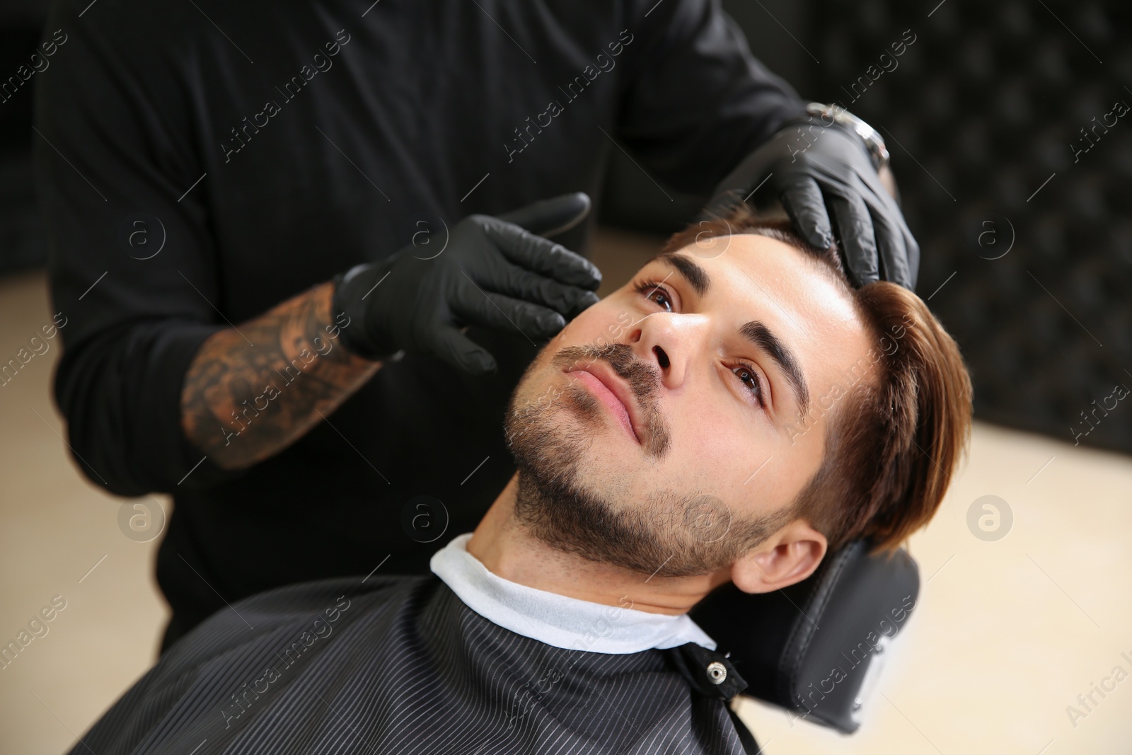 Photo of Young man visiting barbershop. Professional shaving service