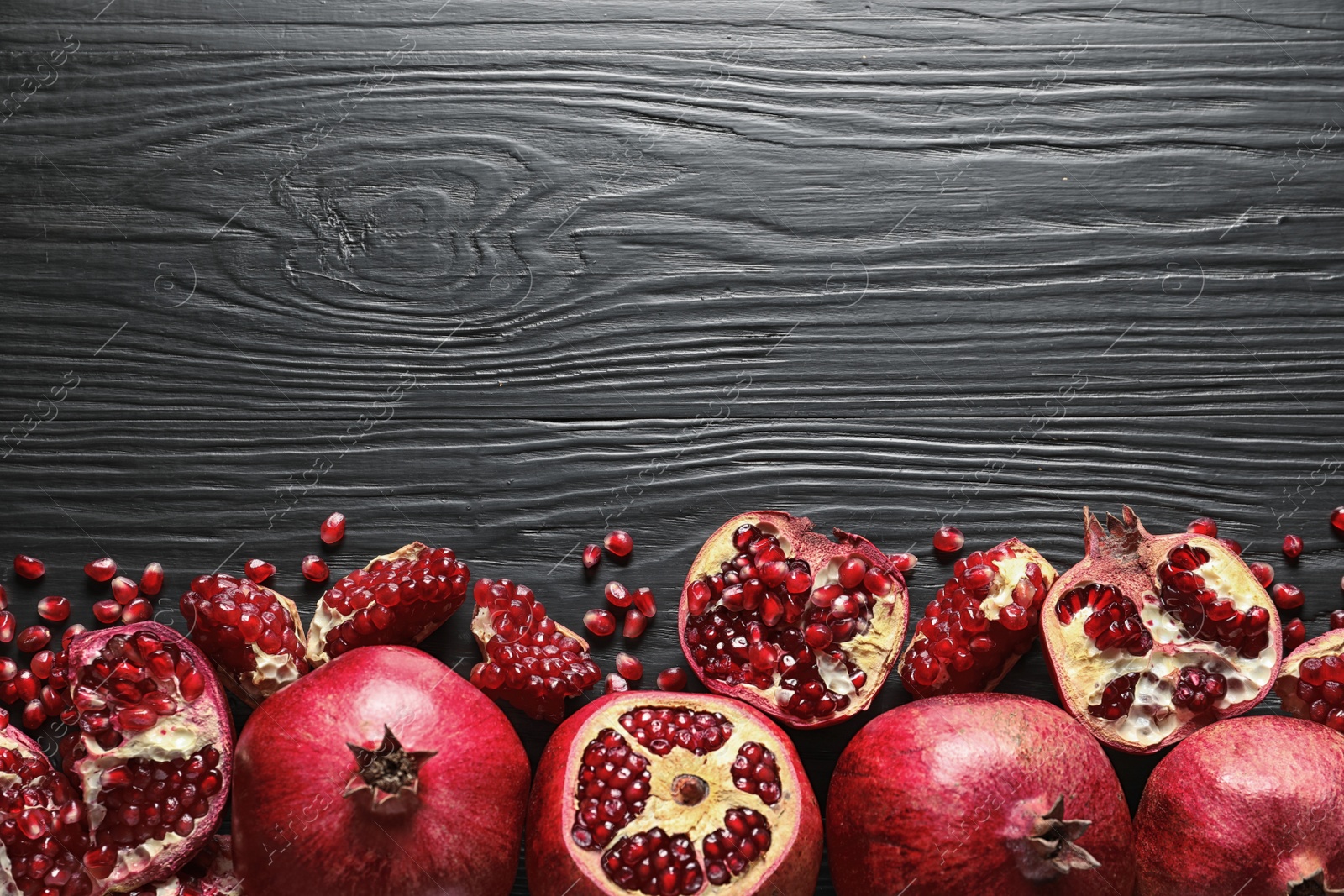 Photo of Ripe pomegranates on dark wooden background, top view with space for text