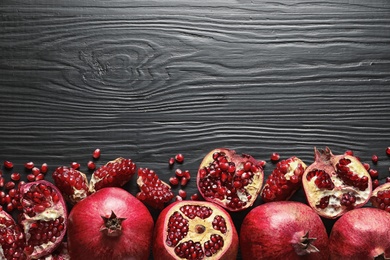 Photo of Ripe pomegranates on dark wooden background, top view with space for text