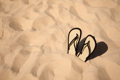 Photo of Flip flops on sandy sea shore, space for text. Beach accessory