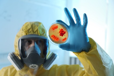 Scientist in chemical protective suit with Petri dish in laboratory. Monkeypox virus