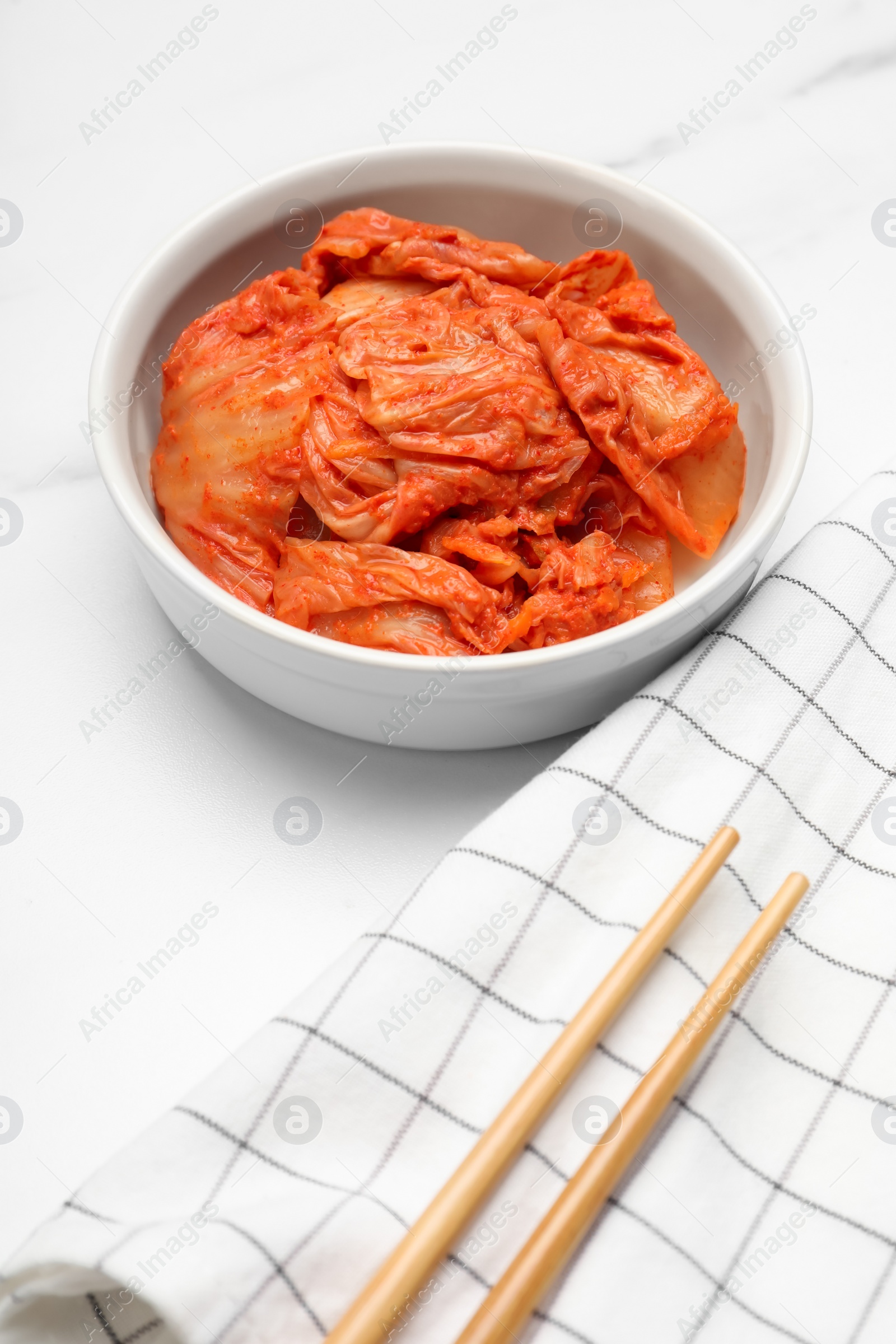 Photo of Bowl of spicy cabbage kimchi and chopsticks on white marble table