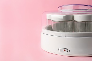 Modern yogurt maker with empty jars on pink background, closeup. Space for text