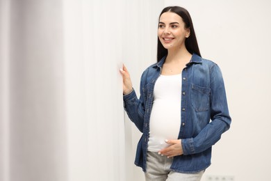 Happy pregnant woman near window indoors, space for text