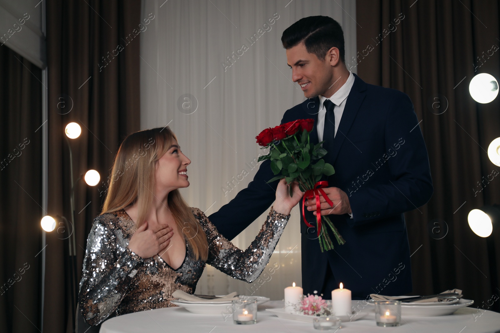 Photo of Man presenting roses to his beloved woman in restaurant at romantic dinner