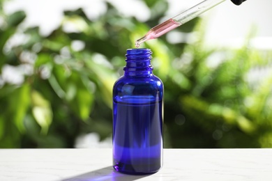 Dropper with essential oil over bottle on white wooden table against blurred background