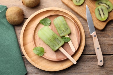 Photo of Flat lay composition with tasty kiwi ice pops on wooden table. Fruit popsicle