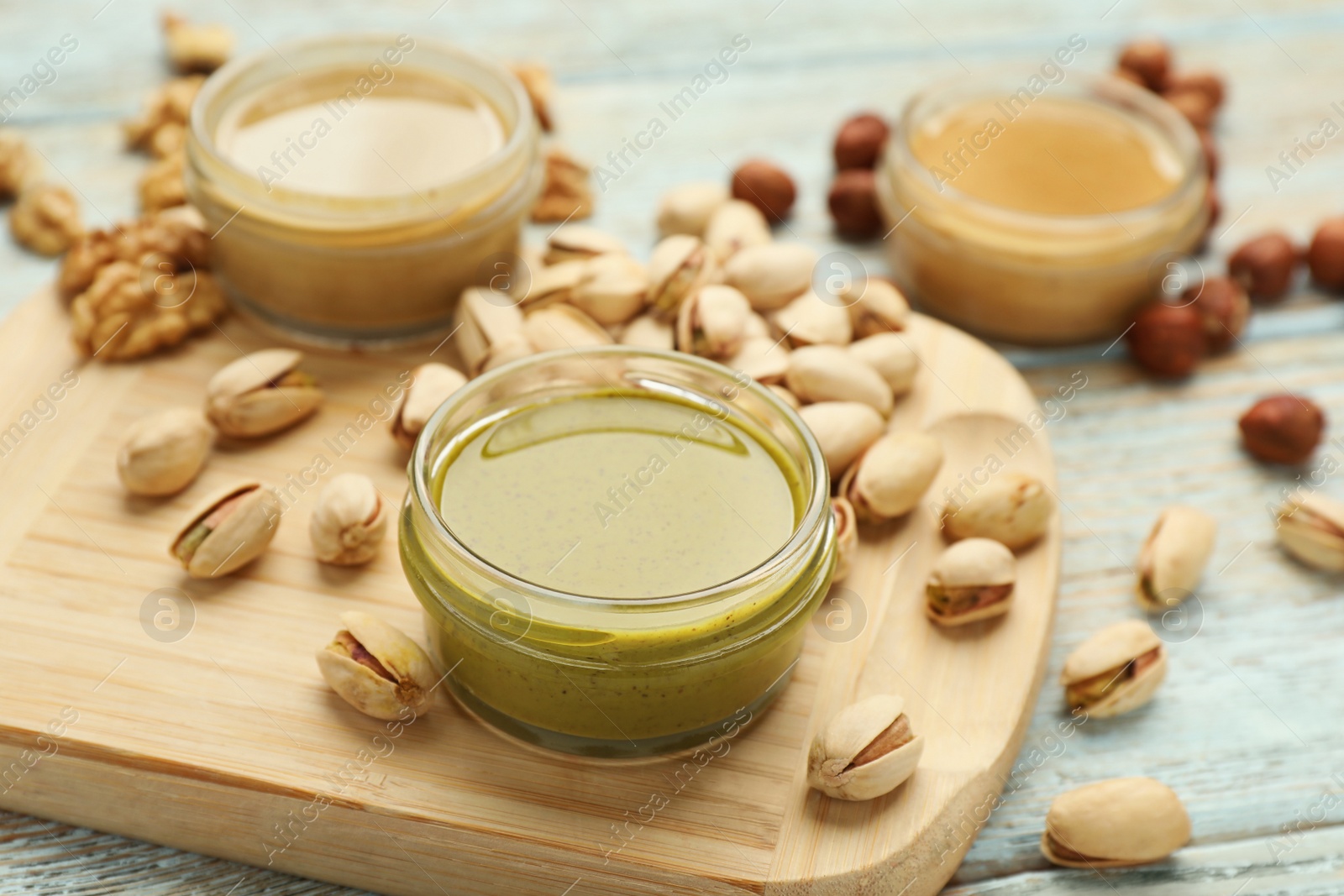 Photo of Different types of delicious nut butters and ingredients on light blue wooden table, closeup