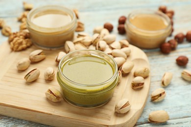 Different types of delicious nut butters and ingredients on light blue wooden table, closeup