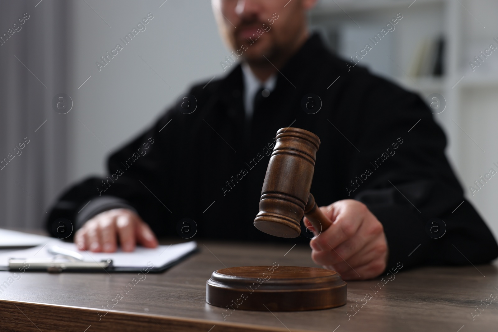 Photo of Judge with gavel and papers sitting at wooden table indoors, closeup