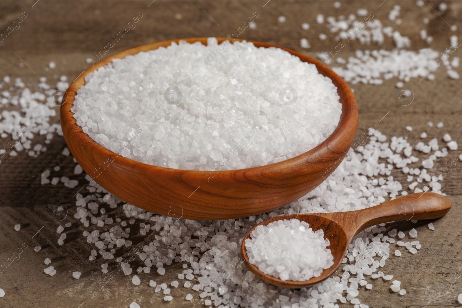 Photo of Bowl and spoon with natural sea salt on wooden table