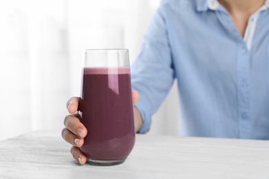 Woman with glass of fresh acai drink at white wooden table, closeup