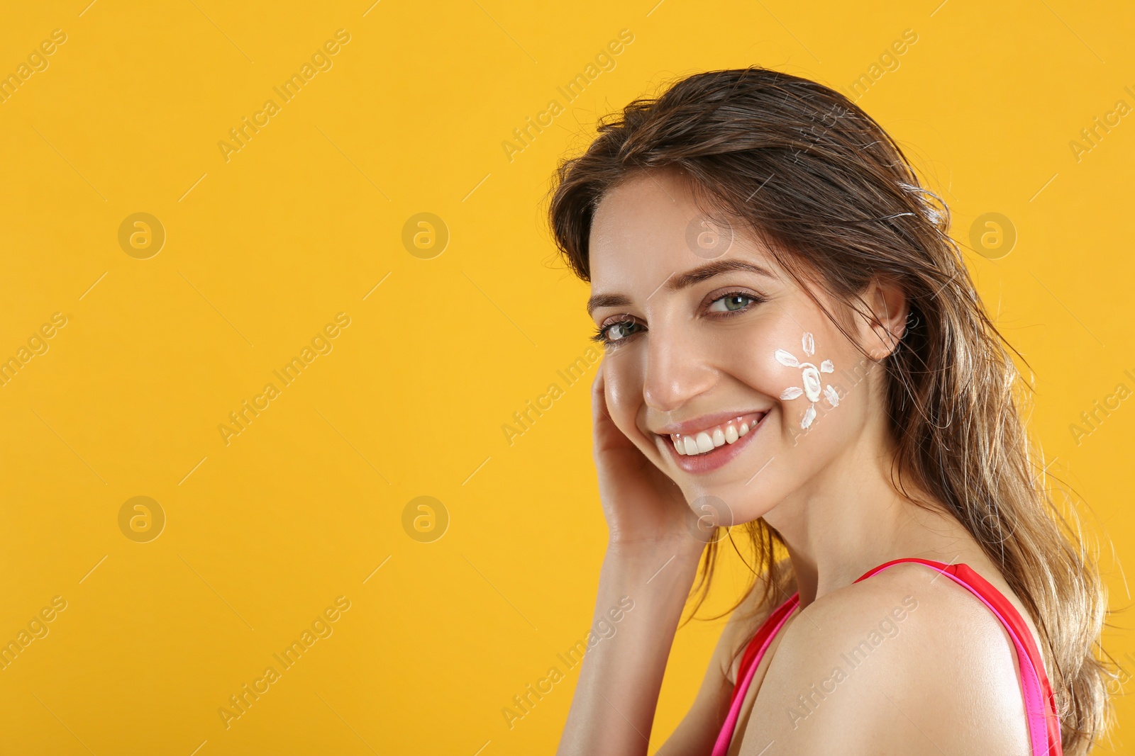 Photo of Young woman with sun protection cream on face against yellow background. Space for text