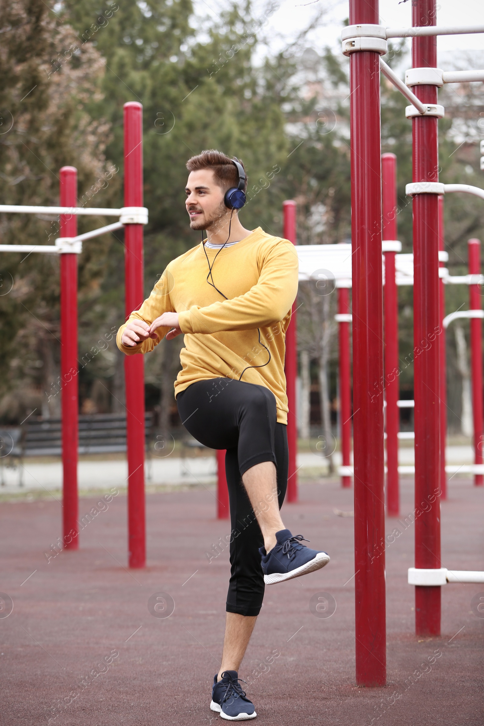 Photo of Young man with headphones listening to music and exercising on sports ground