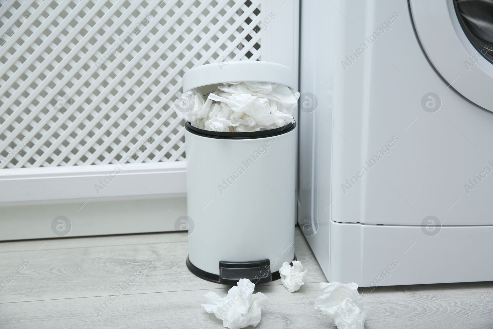 Photo of Used paper tissues in trash can near washing machine indoors