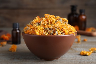 Bowl of dry calendula flowers on wooden table, closeup