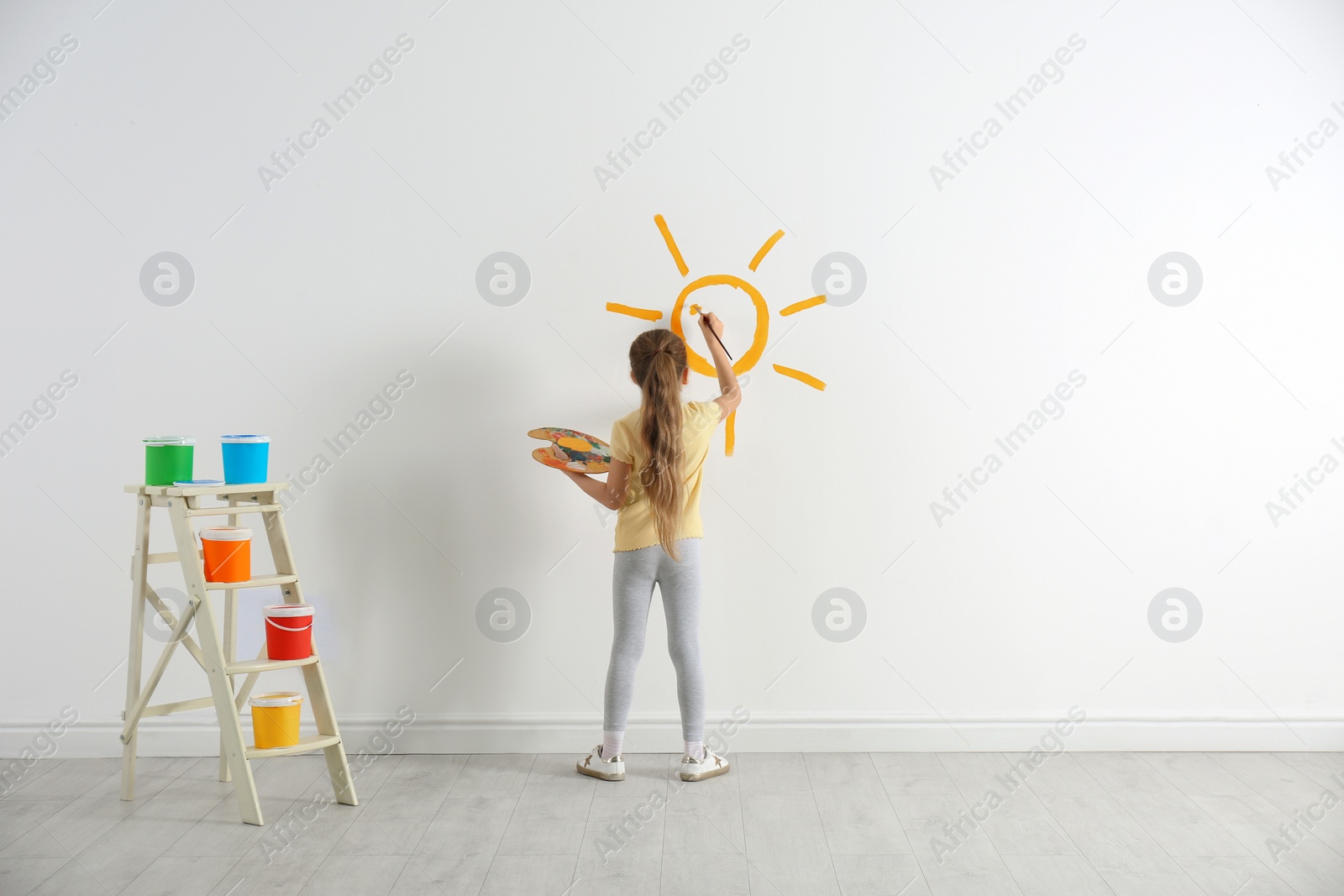 Photo of Little child painting sun on white wall indoors