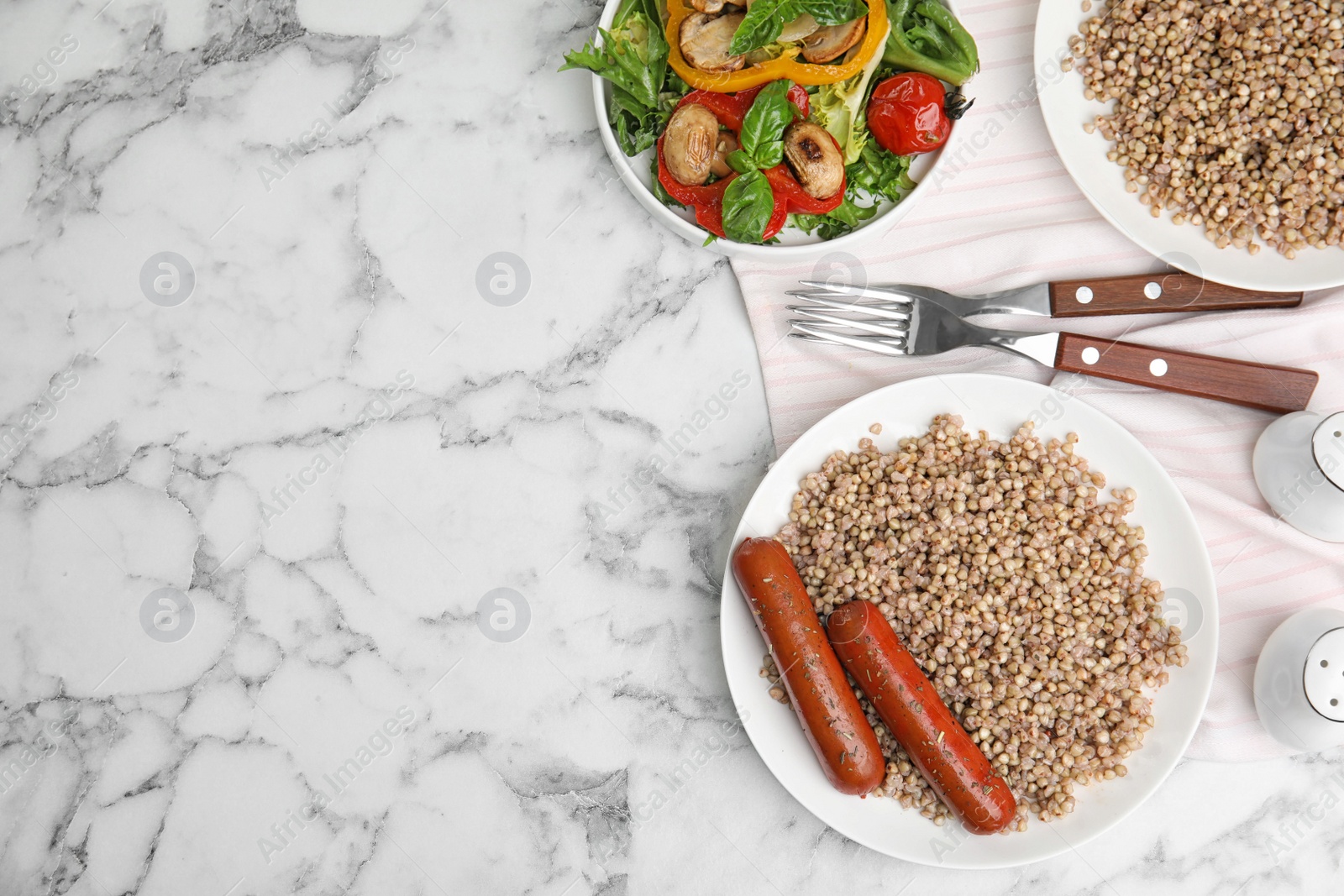 Photo of Tasty buckwheat porridge with sausages on white marble table, flat lay. Space for text