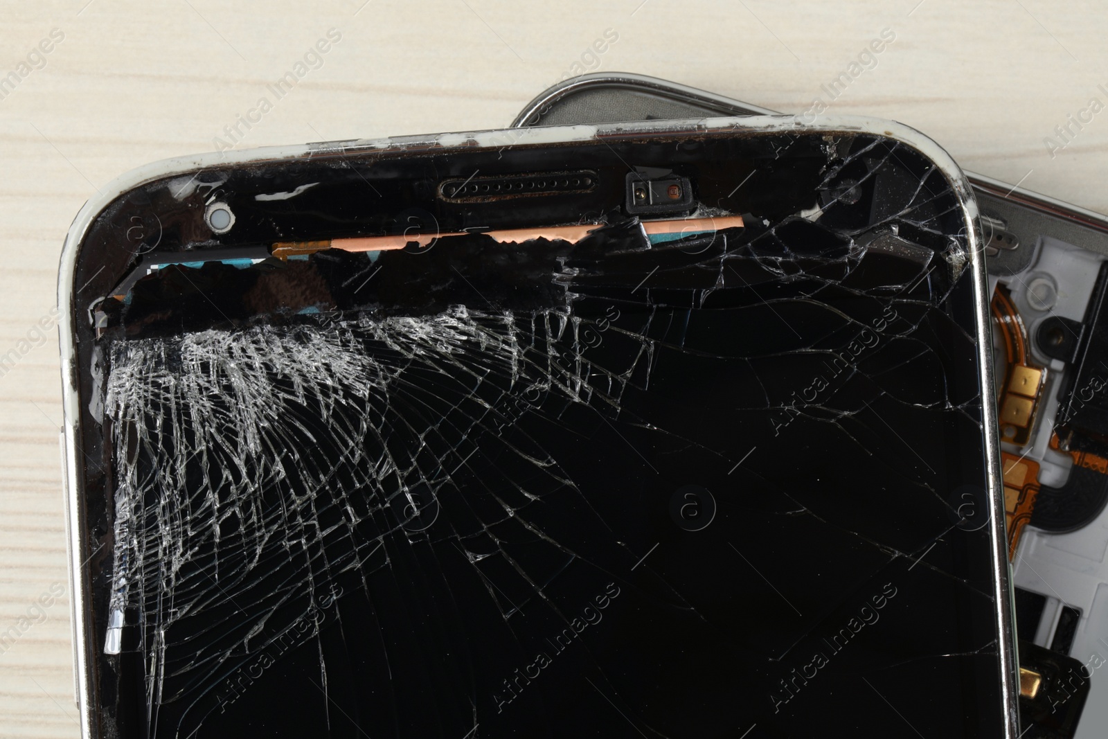 Photo of Broken smartphone with cracked screen on light beige wooden background, top view. Device repair