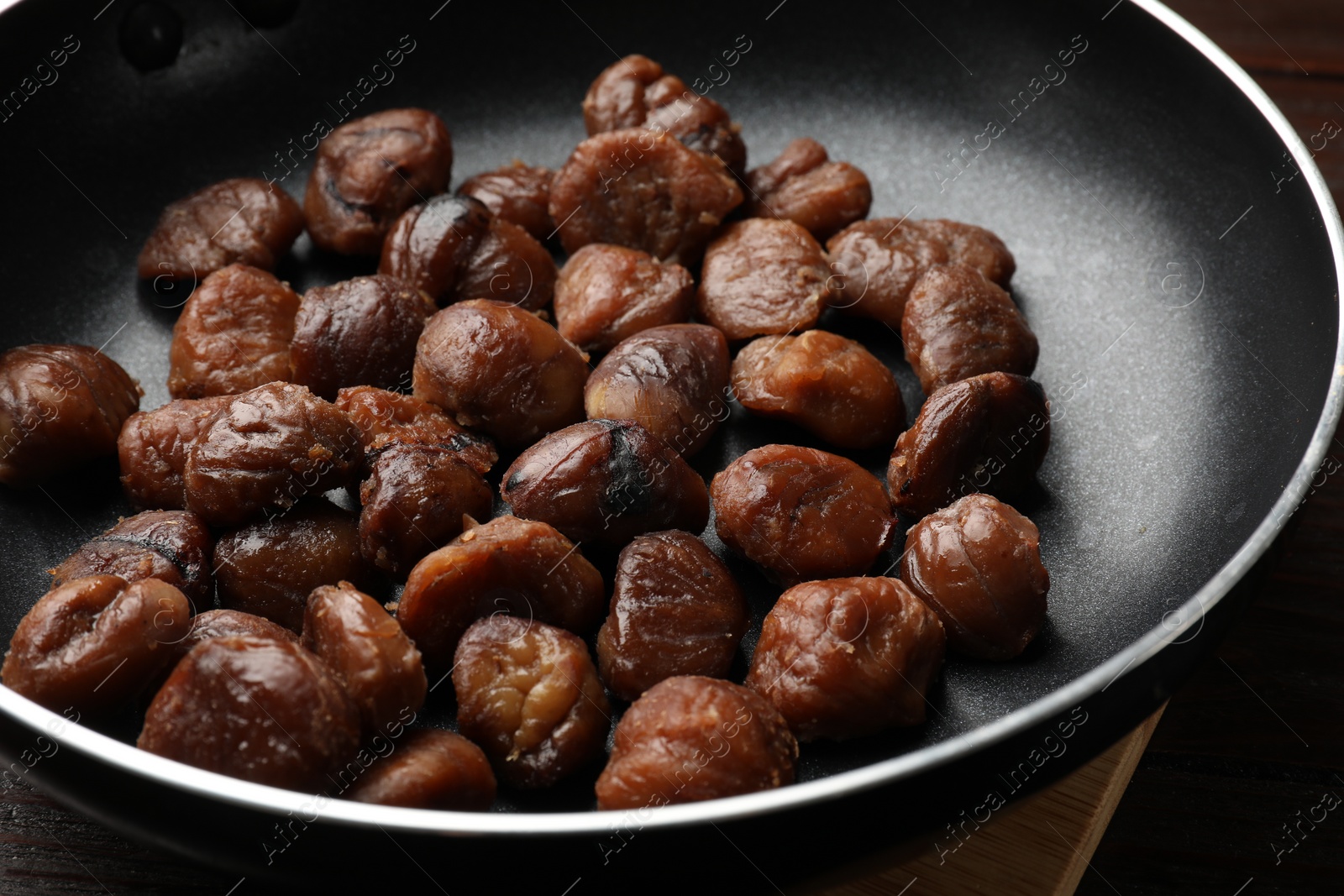 Photo of Roasted edible sweet chestnuts in frying pan on table, closeup