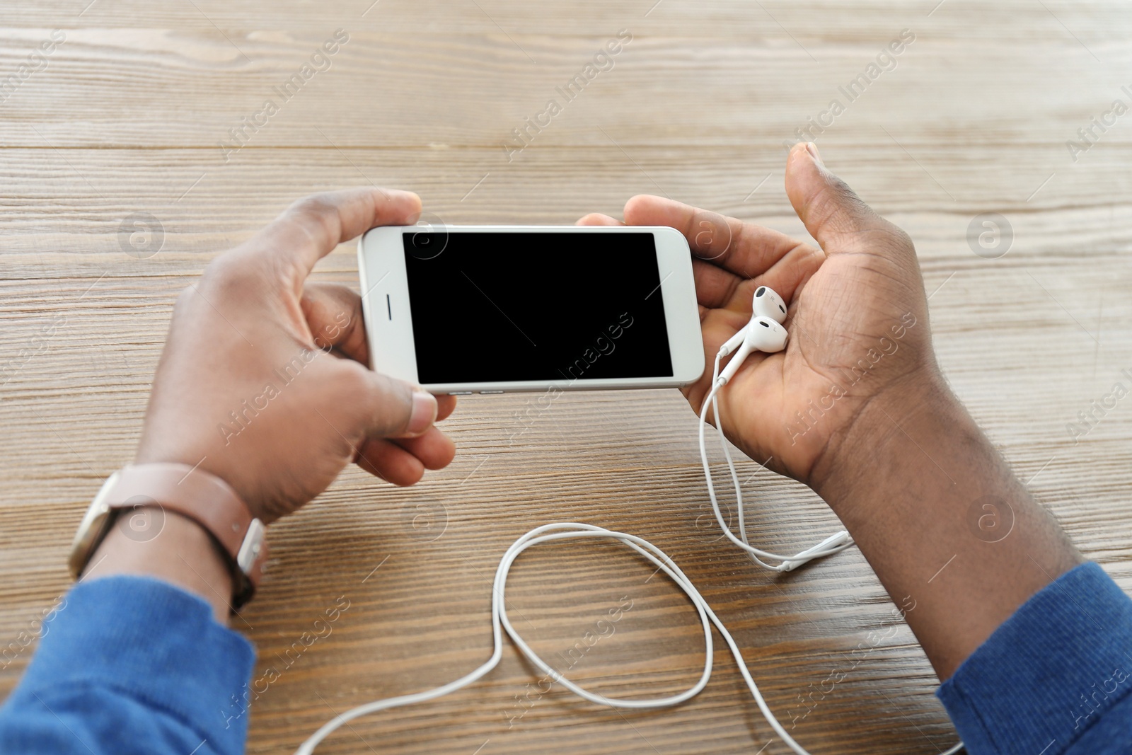 Photo of African-American man holding mobile phone with blank screen in hands at table