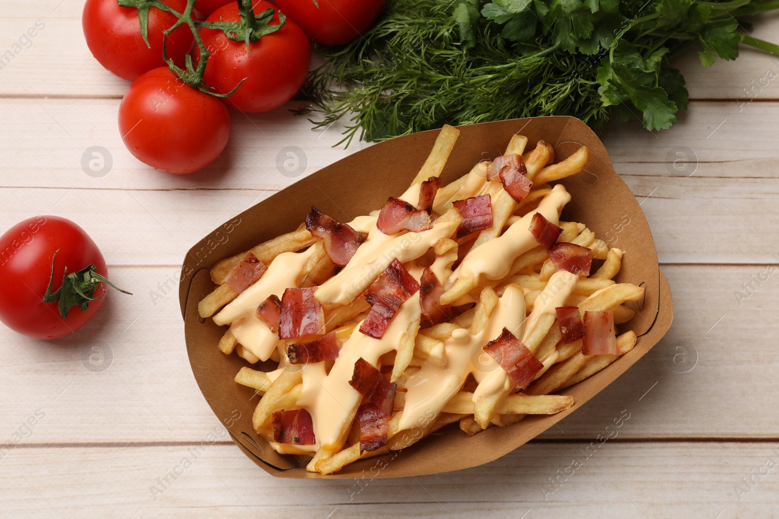 Photo of Tasty potato fries, cheese sauce, bacon and products in paper container on light wooden table, top view