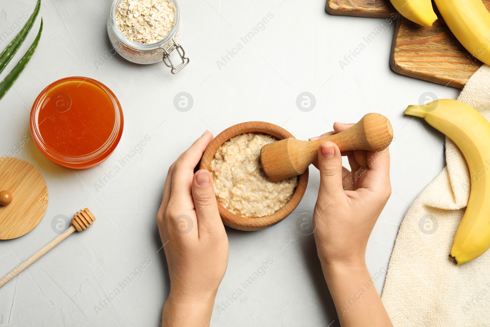 Photo of Woman preparing face mask at grey table, top view. Handmade cosmetic