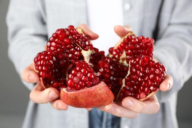 Woman holding fresh pomegranate on grey background, closeup