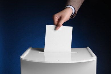 Photo of Woman putting her vote into ballot box on dark blue background, closeup